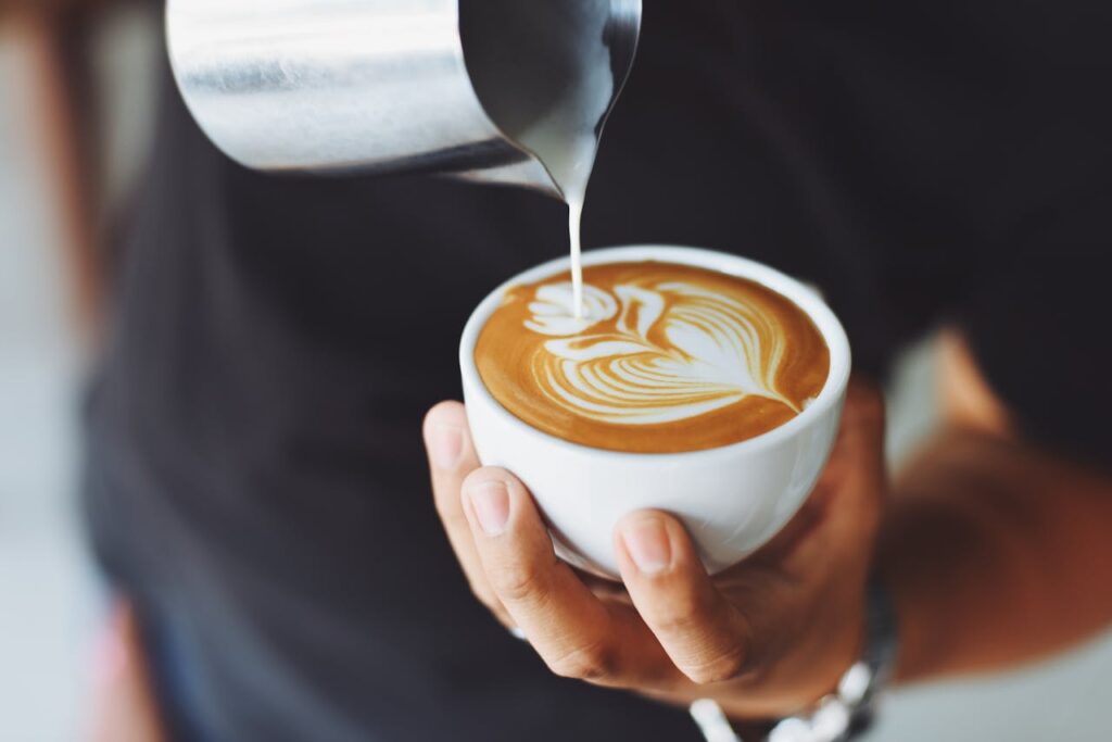 pexels photo 302899 Close-up of a barista pouring milk to create latte art in a coffee cup.